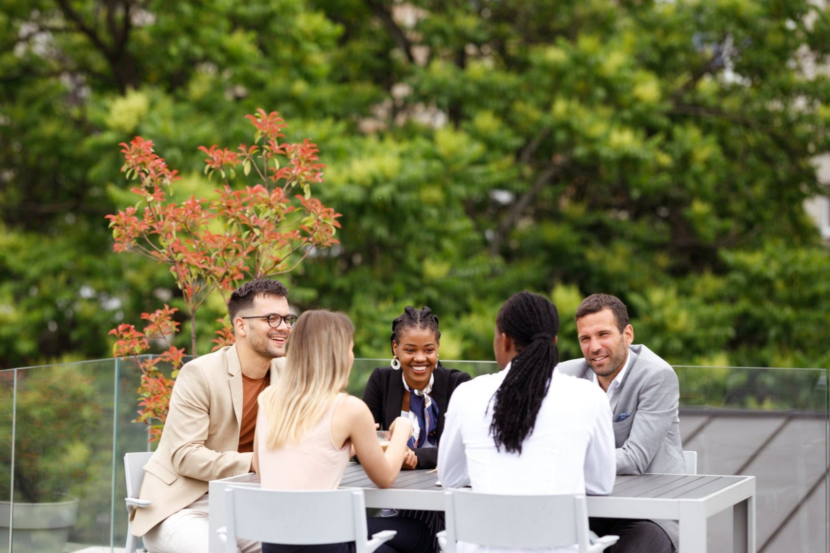 Group of 5 businessmen and businesswomen talking around patio table.